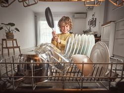 Positive boy with frying pan near dishwasher