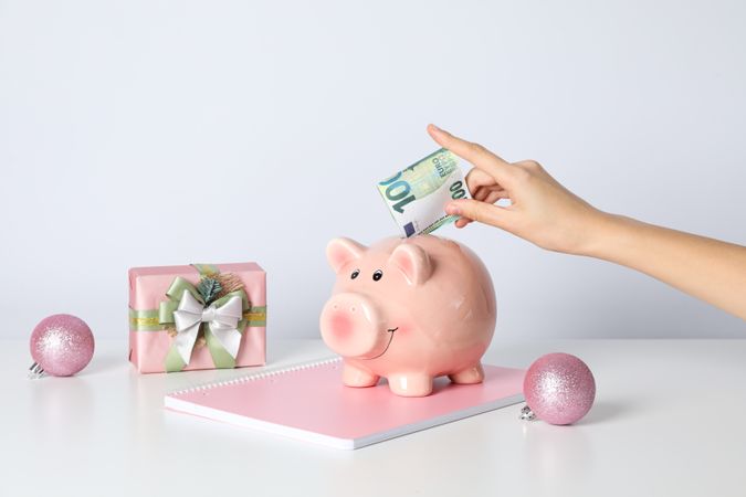Piggy bank, female hand with cash and gift box on blank background