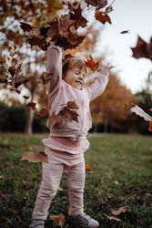 Joyful child scattering leaves on lawn in park