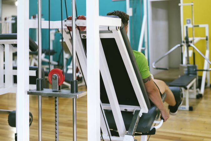 Rear view of healthy male in green t-shirt working out using leg extension machine, copy space