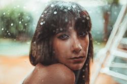 Woman looking at camera behind a wet glass
