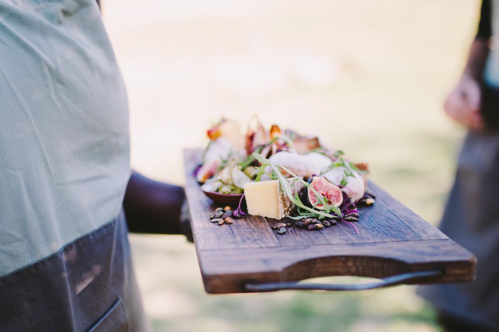 Charcuterie board with cheese, figs and nuts carried by a server
