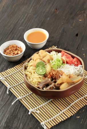 Traditional Indonesian beef noodle soup with noodles, beef, spring roll, cabbage and tomato