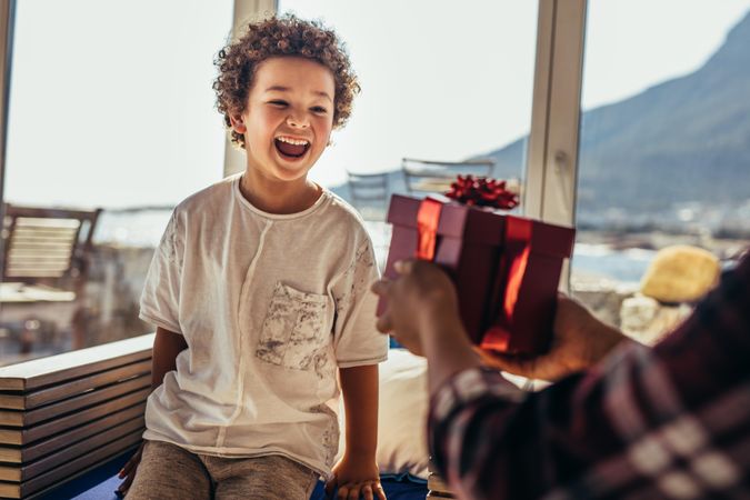 Person giving a gift box to a boy sitting in a beach house