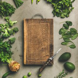 Arrangement of fresh green garden vegetables on concrete surface, with wooden board, square crop