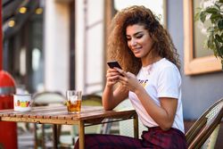 Arab woman in casual clothes texting using her phone on cafe patio