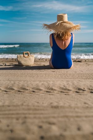 Woman in blue swimsuit and hat on sandy beach