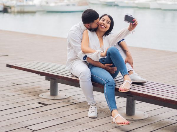 Woman with man taking photo selfie and kissing on bench