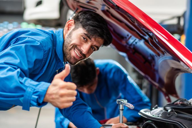 Happy male mechanic giving thumbs up while checking car engine