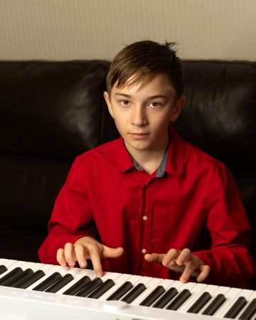 Teen boy playing piano, fingers pressing the keys.