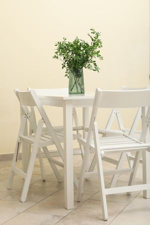 Wooden table with vase with plant and folding chairs against light beige wall