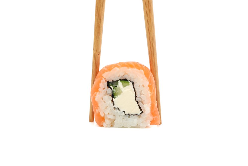 Chopsticks with sushi roll isolated on plain background