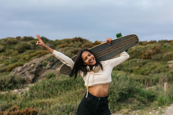 Joyful woman standing with longboard behind head