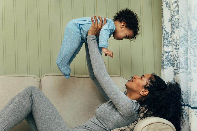 Mother lying down holder her toddler son above her head