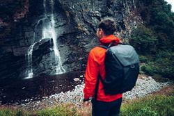 Back view of a man in red jacket with backpack standing near waterfalls 48Q8kb