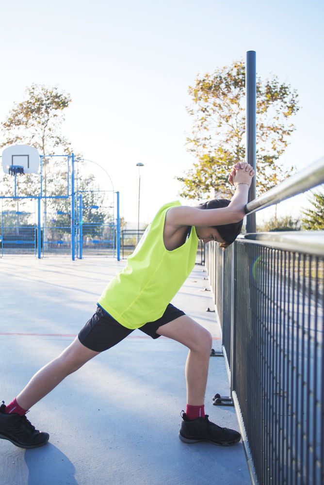 Side view of a young basketball player stretching legs before playing game outdoors