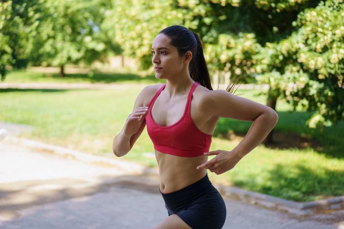 A woman is jogging in a park on a sunny day, dressed in sportswear
