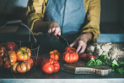 Woman in yellow chopping large tomatoes on wooden board