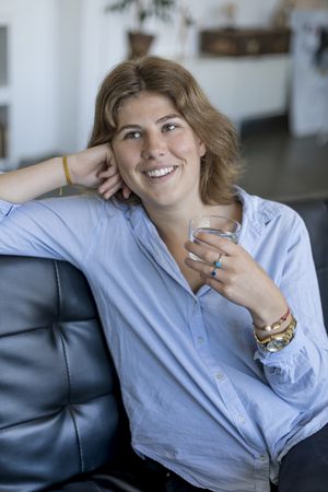 Attractive young woman sitting on couch and holding glass of water