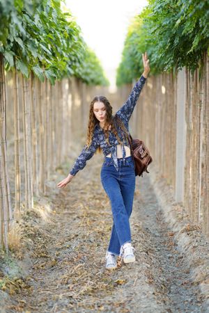 A stylish young woman dances joyfully in a scenic vineyard, surrounded by vibrant nature