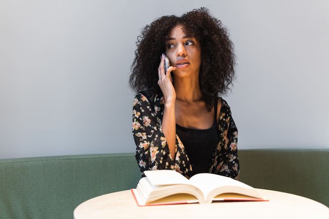 Black woman speaking on smartphone at table with book
