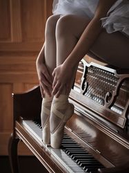 Crop ballerina sitting on piano and pushing keys with feet