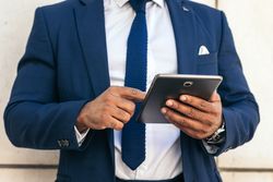 Unrecognizable Black businessman in a suit using a tablet outside.