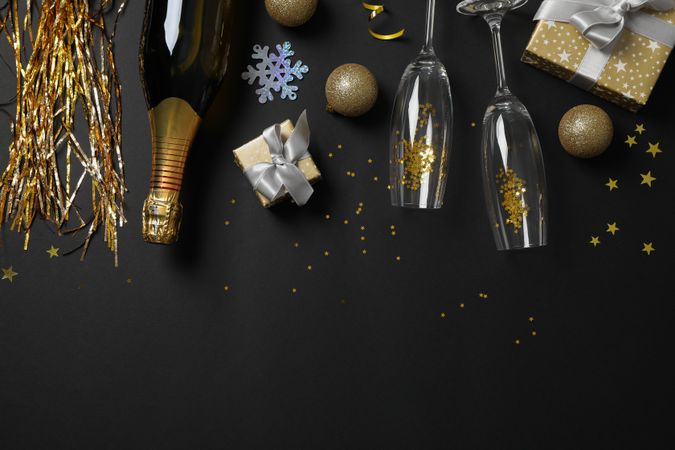 Champagne bottle, glasses and christmas baubles on dark background, copy space