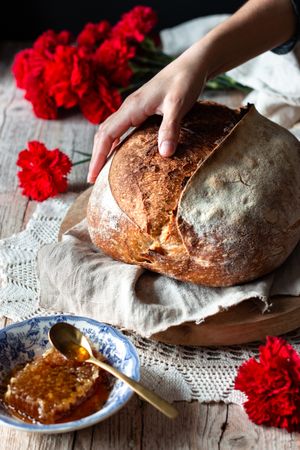Crop person putting sourdough bread near flowers and honey