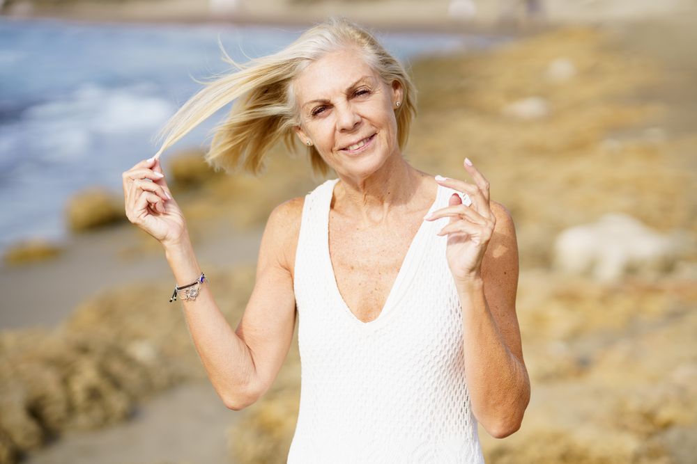 Older woman with grey hair moving hair off her face in the wind on the coast