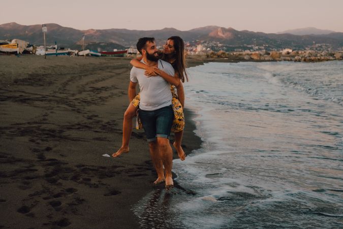 Amorous man carrying woman on arms along sandy beach