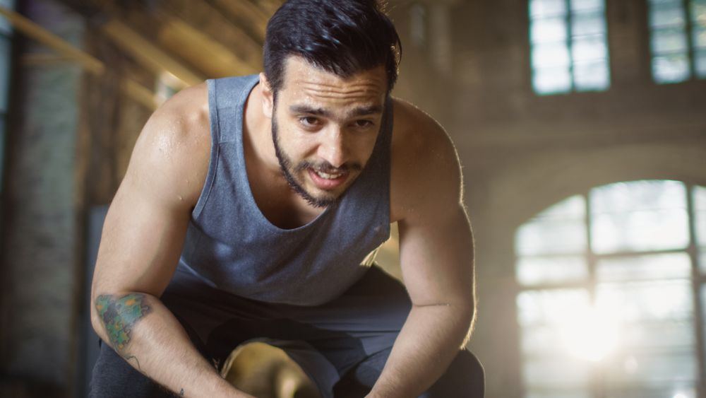 Exhausted Bend Muscular Man Rests After Intensive Workout.