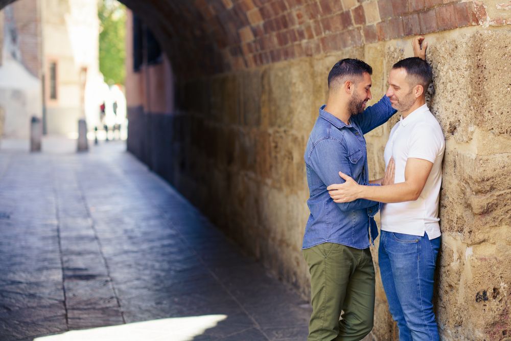 Two men facing each other and embracing under a city bridge