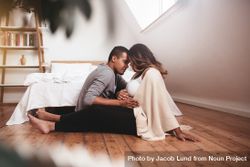 Romantic young couple sitting on floor of bedroom holding mother’s belly 0WrXPb