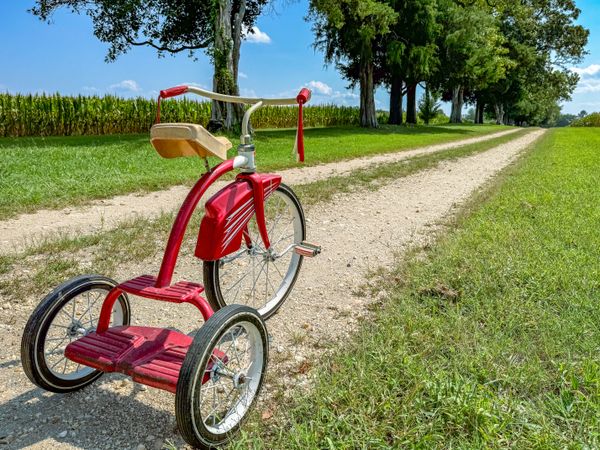 Red tricycle with tassels on farm road