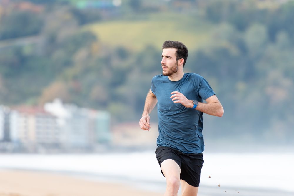 Sportsman in active wear jogging on lonely beach