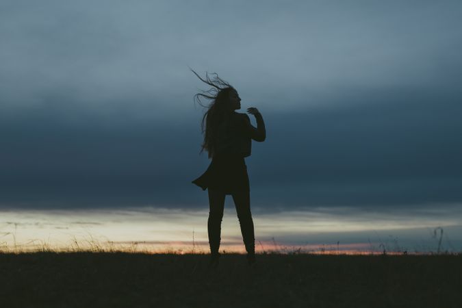 Woman standing in a field at dusk with her hair blowing back