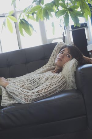Female in wooly sweater relaxing on leather couch in living room, vertical