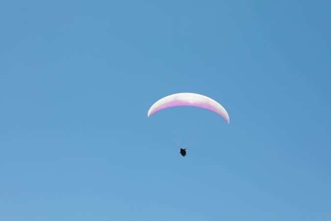 Skydiver with a pink parachute flies across the blue sky