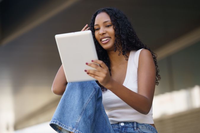 A young woman is engaging with her tablet in a relaxed and casual outdoor setting