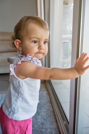 Cute baby girl leaning on window at home