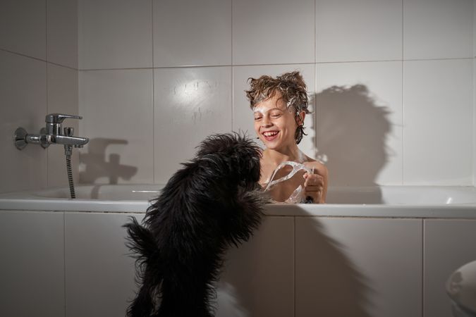 Happy boy washing in bathtub near dog