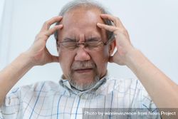 Older male with his hands holding his head in pain bGkV2b