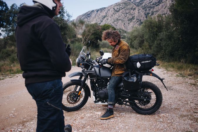 Two men with a motorcycle near a hill