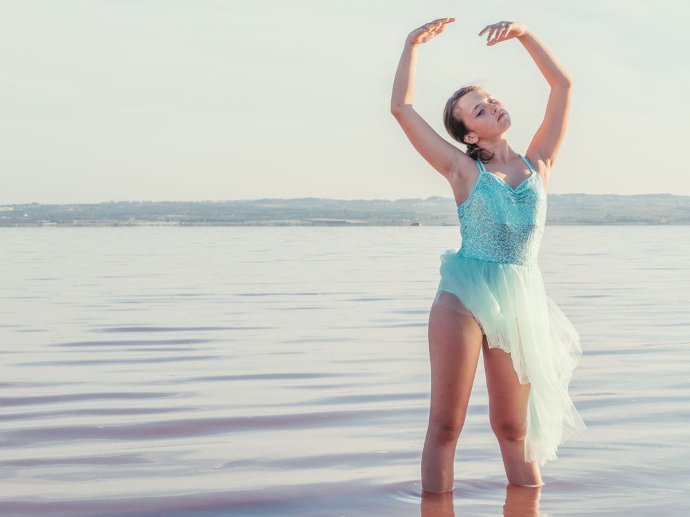 Ballerina in swimsuit with tutu performing classical position in water