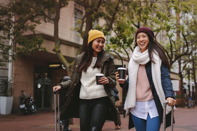 Two young Asian women in winter clothes walking with coffees