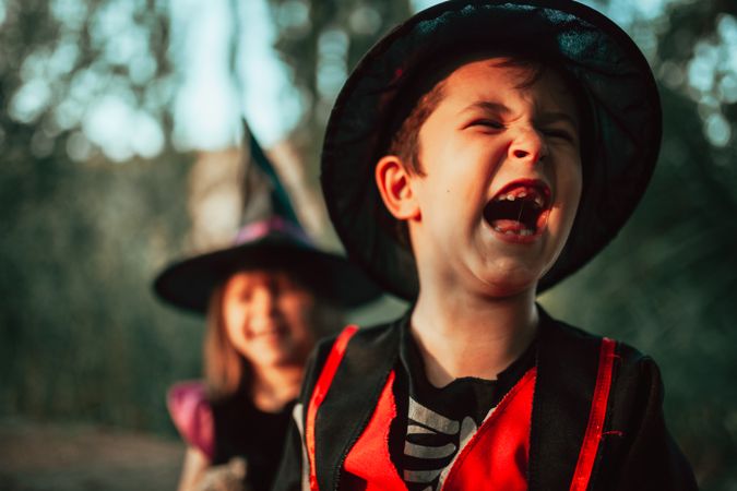 Boy howling with laughter in halloween costume with sister in background