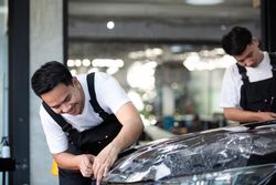 Two Asian detailing a vehicle with a protective wrap