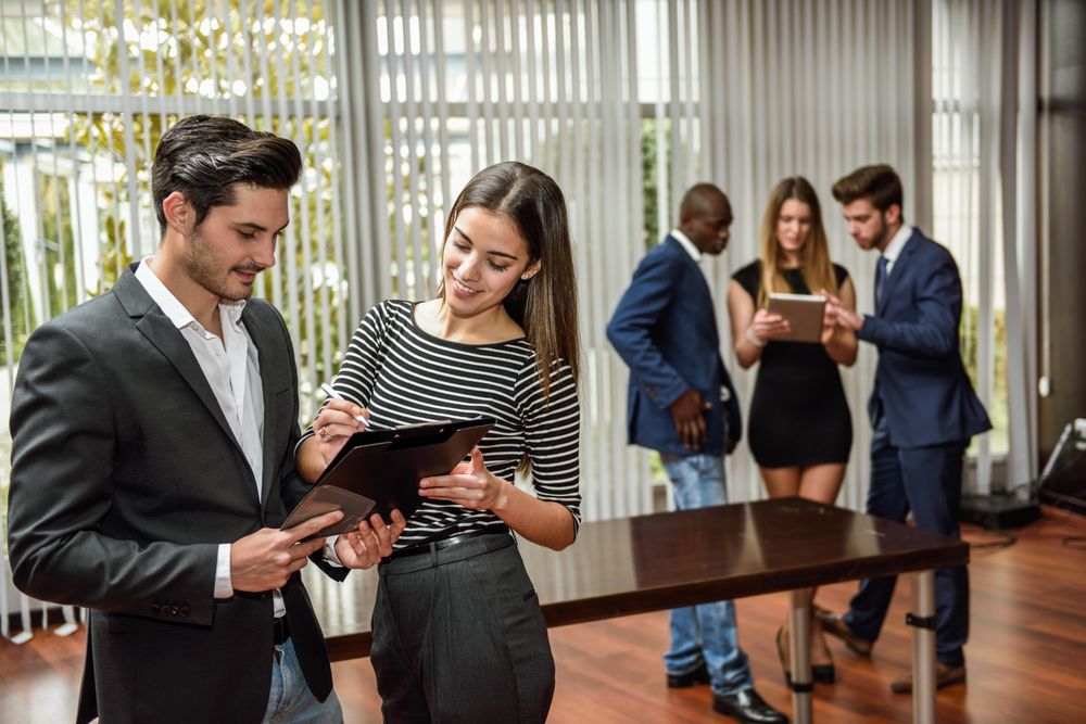 Two colleagues referring to clip board in busy office