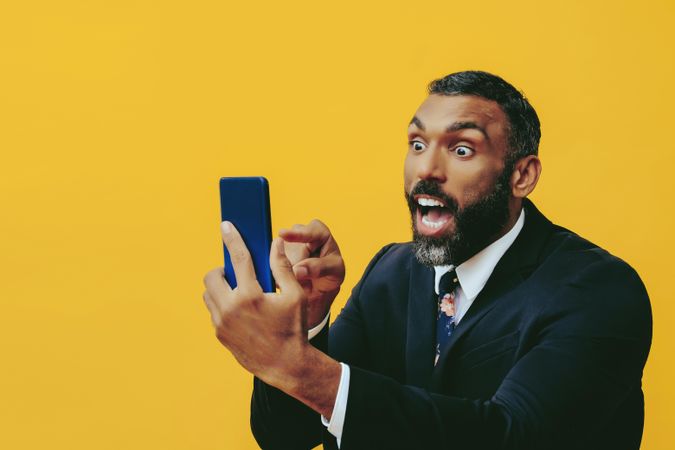 Energetic Black businessman in suit yelling at smartphone screen while pointing